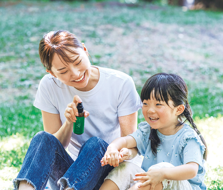 緑豊かな屋外で、母親が子供の腕に森の肌守り。をスプレーしている様子